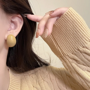 Close-up of a model wearing yellow resin geometric C-shaped stud earrings in a warm light
