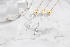 Close-up of S925 sterling silver cross earrings on a white marble background with flowers