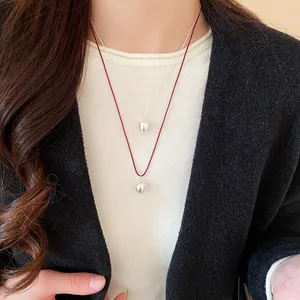 Detail of layered apple pendants with red leather cord and silver chain on a tweed jacket