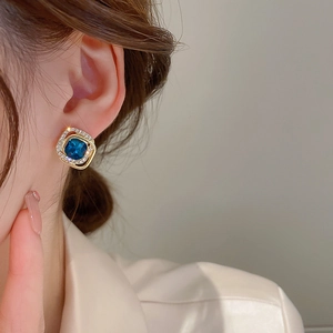 Close-up of square blue crystal stud earring with double-layered gold diamond frame