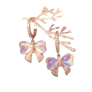 Elegant rose gold bow earrings with iridescent pendant hanging on a golden display branch