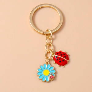Detail showing ladybug and blue flower metal pendants on a gold keychain chain