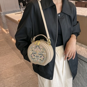 Detail view of a beige round crossbody bag with exquisite floral embroidery and gold hardware