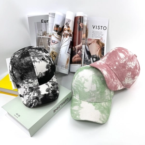 Détail de casquettes tie-dye en vert, rose et noir marbré posées sur des magazines