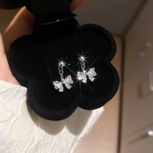 Sparkling zircon bowknot earrings displayed in a black flower jewelry box with light glares