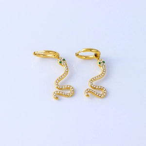 Macro detail of 18K gold snake earrings with white cubic zirconia and green gem eyes