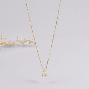 Detail of a minimalist 18K gold chain necklace with a pear-shaped clear stone pendant
