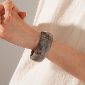 Macro detail of wide resin bangle with brown marble texture on a model's wrist