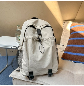 Detail eines beigen Nylon-Rucksacks auf dem Sofa mit Netztaschen und verstellbaren Gurten