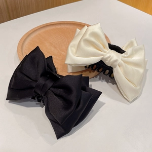 Detail of large satin bow hair claws in black and beige with glossy silk texture