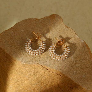 Golden C-shaped earrings with layered white pearls on a textured rock background