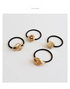 Detail display of four black elastic hair ties with diverse gold metal accents and knots