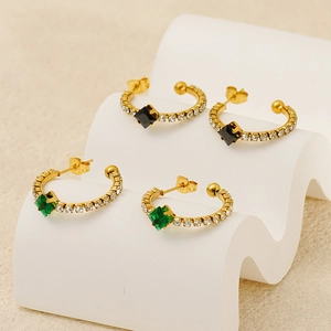Close-up of vintage gold C-shaped earrings with rhinestones and black or green square gems