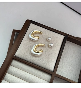 Detailed macro view of gold-plated geometric C-shaped earrings and white pearl studs