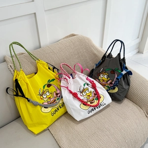 Three embroidered nylon tote bags in yellow, white, and grey on a cozy fabric sofa