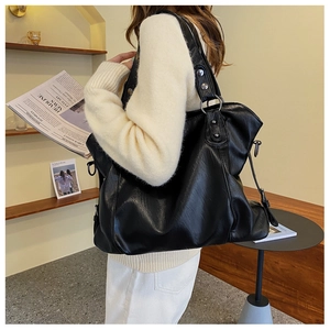 Detail of a large black leather tote bag with metallic ring and soft texture on a model
