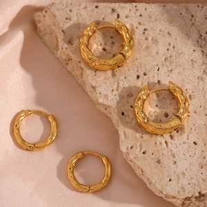 Detail of golden stainless steel earrings with irregular hammered texture on rock and silk