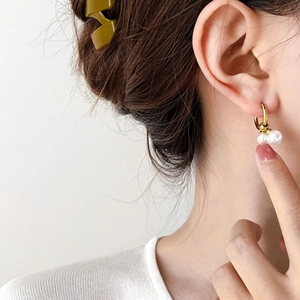 Elegant gold titanium earrings featuring a double pearl drop design worn by a model