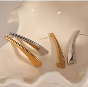 Detailed macro view of polished gold and silver triangular earrings on a shell stand
