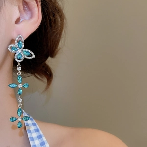 Detail of silver butterfly tassel earrings featuring blue rhinestones on a model