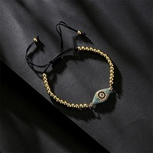 Macro detail of copper evil eye bracelet with gold beads and black braided cord