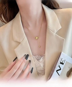 Detail of a gold titanium necklace with a polished sphere and bar pendant on a model