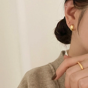 Macro view of minimalist golden stud earrings and ring set on model in brown knitwear