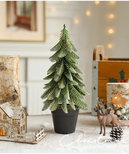 Close-up of mini snowy Christmas tree in black pot with festive warm lighting