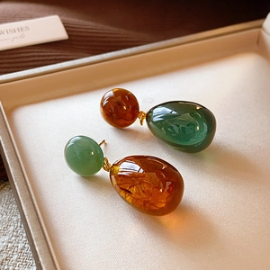 Close-up of asymmetric resin teardrop earrings in amber and dark green on beige leather box