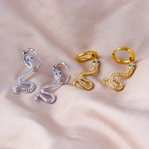 Close-up of gold and silver snake earrings with pavé zircons and green gem eyes