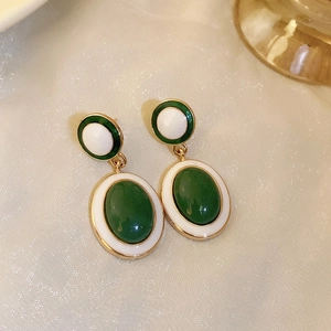 Close-up of vintage gold earrings with green and white oval resin stones on fabric