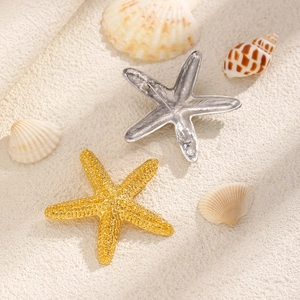 Detail of gold and silver starfish brooches on white sand with sea shells for beach style