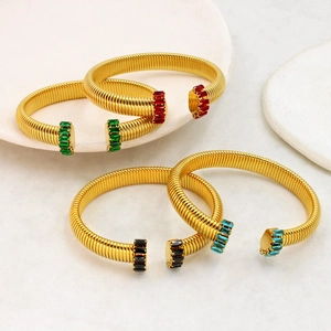 Dettaglio di bracciali a spirale dorati con zirconi colorati e design a forma di C