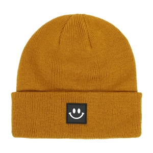 Dettaglio del berretto in maglia giallo senape con toppa nera quadrata a forma di smiley