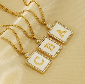 Detail of square gold pendants with A, B, C letters, white enamel and crystals