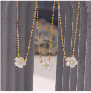 Detailed view of white mother of pearl flower pendants with gold bead chains on stone stand