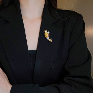 Detailed view of a golden fish brooch with pearls and zircons on a black blazer suit