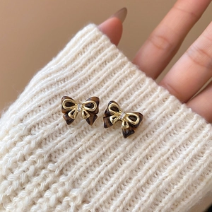Detailed close-up of bow earrings with brown tortoiseshell texture and gold metal trim