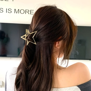 Dettaglio di un mollettone a stella dorato Y2K acconciato su capelli lunghi per un look trendy