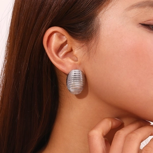 Close-up of a silver ribbed oval stud earring in stainless steel worn on the earlobe