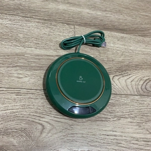 Top view of a green USB cup warmer with gold trim and heating cup text on a wood surface