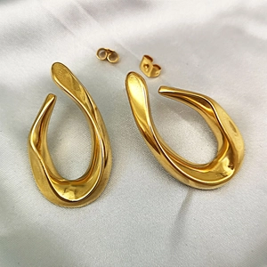 Macro detail of high-polish 18K gold-plated fluid metal drop earrings on white silk