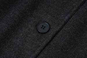 Detailed close-up of a black four-hole button on thick dark grey wool coat fabric
