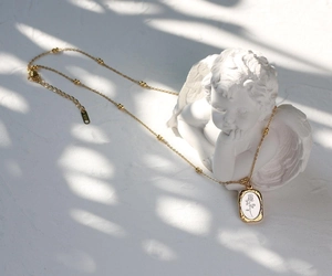 Detail of vintage French style gold necklace with rose pendant on an angel statue