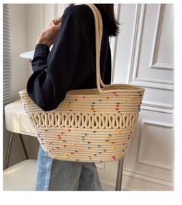 Detail of a beige woven tote bag with colorful dots worn on the shoulder by a model
