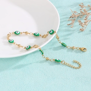 Detail of gold evil eye bracelet with green enamel beads and lobster clasp on white plate