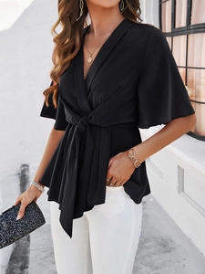 Détail d'un haut noir chic à col en V avec ceinture nouée et accessoires dorés élégants