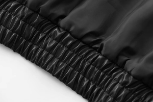 Detail of the elastic ribbed hem and premium faux leather texture on black bomber jacket