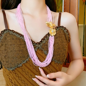 Detail of multi-layer pink seed bead necklace with a golden flower pendant on model
