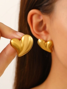 Detailed close-up of matte gold heart-shaped stud earring worn on ear and held in hand